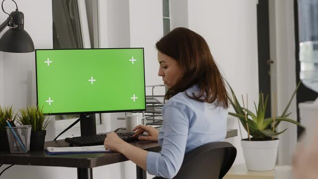 Executive assistant analyzing green screen template on computer, checking isolated display on pc in coworking space. Woman using blank chroma key copyspace screen, professional agency.
