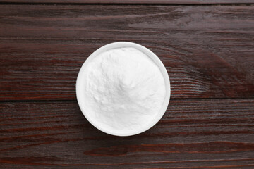 Bowl of sweet powdered fructose on black wooden table, top view