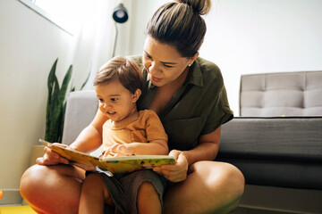 Mom reading a book with baby boy at home. Early age children education, development. Mother and child spending time together. Candid lifestyle.
