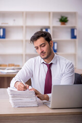 Obraz premium Young male employee and too much work at workplace