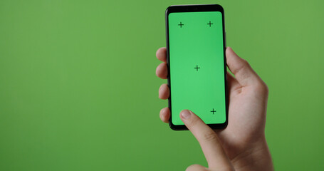Close up of man's hand holding a smart phone with vertical green mock up chroma key screen and doing gestures on touchscreen 