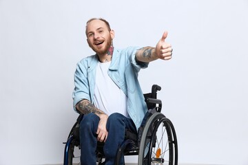A man in a wheelchair looks at the camera shows a thumbs up, happiness, with tattoos on his hands...