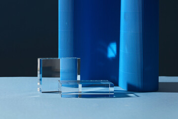 Two transparent geometric blank podiums decorated on dark background. Blue paper corrugated to...