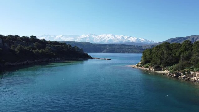 Bird's Eye View Of Drone Flying Low Between Small Islands. The White Mountains of Crete (Lefka Ori) Full Of Snow In The Background.