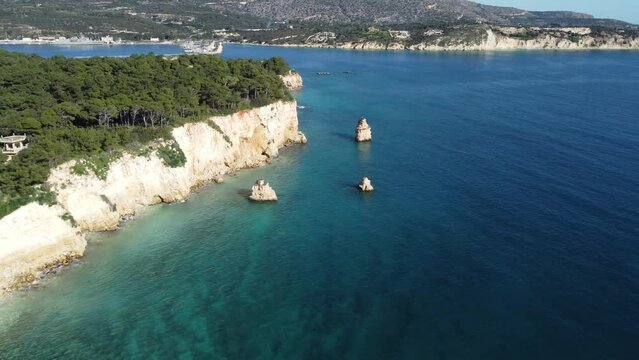 Forward moving aerial view over small tree island. Dense forest over the cliffs. Turquoise Sea Water. Souda Crete Greece