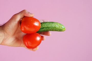 A man's hand holds two tomatoes and a cucumber. The concept of the problem of sexual health of men....