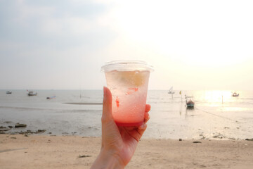 Hand holding strawberry lemon soda in take away cup (plastic glass) on the beach background.