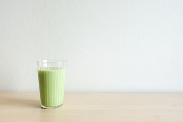 Homemade iced green matcha tea and milk in glass on wooden table.