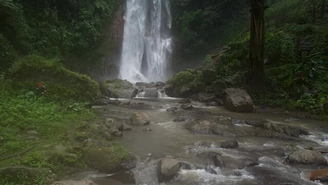 Low angle dolly shot over flowing stream and falling Gitgit Waterfall in background - Jungle of Bali,Indonesia