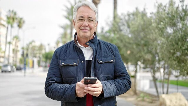 Middle age man with grey hair using smartphone smiling at park