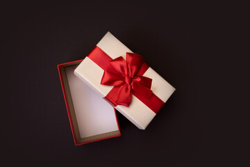 Open gift box with red bow on black background