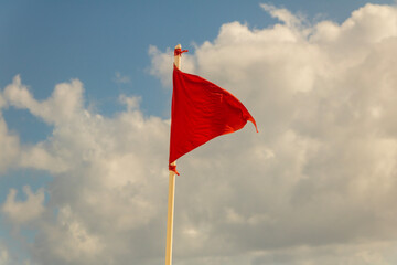 A red flag on a white pole waving in the wind on a sandy beach next to the ocean in Cancun, Mexico.