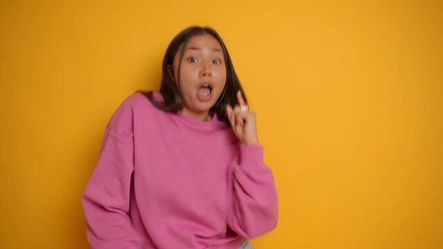 Beautiful brunnete with long hair posing against yellow background in pink sweatshirt, dancing and making hand movements, smiles happily, lucky time concept, high quality video