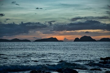Naklejka na ściany i meble Picturesque sunset at the sea of El Nido, Palawan in the Philippines, the sky shines in golden orange and yellow tones, hills in the background.