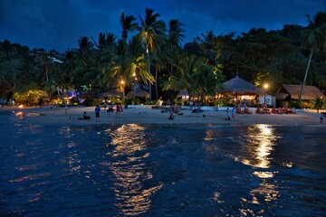 Sandy beach of El Nideo, Palawan in the Philippines at night, with illuminated palm trees and huts.