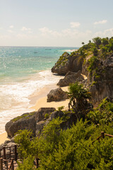 A vertical image of a tropical paradise beach with cliff surrounding it and ocean waves on the other side on a sunny summer day.