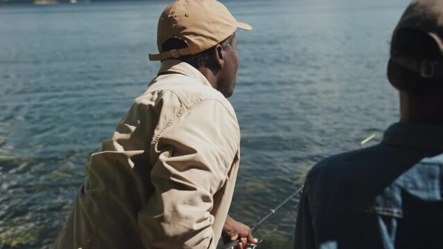Selective focus shot of African American senior man teaching his grandson how to cast fishing rod with bait and and hook