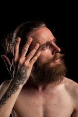 Obraz premium Portrait of cool tattooed bearded guy on black background in studio photo. Expression and fashion