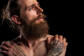 Portrait of tattooed bearded hipster guy on black background in studio photo. Expression and fashion