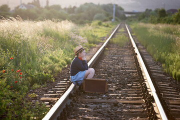 A little girl in a dress sits on an abandoned railroad tracks