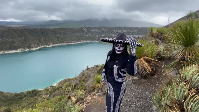 Person posing as a Mexican Day of the Dead skull catrina overlooking a lake on a stormy day.