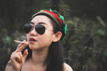 Yong Asia woman smoking marijuana at cannabis tree plant background