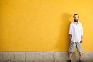 Obraz na płótnie Canvas Tattooed bearded hipster on yellow wall posing outdoor