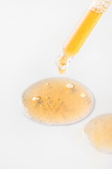 Dropper pippete pouring liquid on white background with other orange round drops smear. Cosmetic,medicine, labaratory test and pharmacy concept.