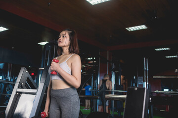 A young asian woman does cross body hammer curls with a pair of pink rubberized dumbbells. Working out biceps at the gym.