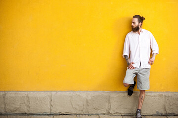 Cool tattooed bearded hipster on yellow wall posing outdoor