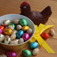 Chocolate hen fo Easter with eggs wrapped in multicolored foil on wooden table