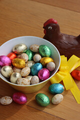 Chocolate hen fo Easter with eggs wrapped in multicolored foil on wooden table