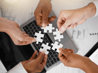 Hands, puzzle and overhead with a business team in the office, working in collaboration on a project. Teamwork, jigsaw piece and laptop with a diverse group of people at work together from above