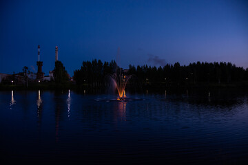 Fototapeta na wymiar Beautiful well-maintained modern park in the city of Kuvshinovo, Tver region at night. Multi-colored fountain in the Osuga River near Kuvshinovskaya BKF.