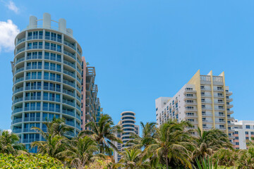 Fototapeta na wymiar Modern hotels apartments with balconies against the blue skies in Miami, Florida. There are buildings on the left with round walls near the building on the right with yellow trims.