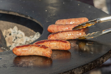 Pork sausages ready to eat, grilled or roasted in a barbecue on an open fire and flames, in a street food market or an outdoor picnic, close up