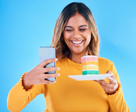 Woman, cake and smile selfie in studio for social media profile picture and excited to eat. Happy female laughing on blue background with rainbow color dessert for birthday or influencer celebration