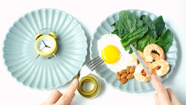 Plate with food and plate with an alarm clock on white background top view, intermittent fasting concept.