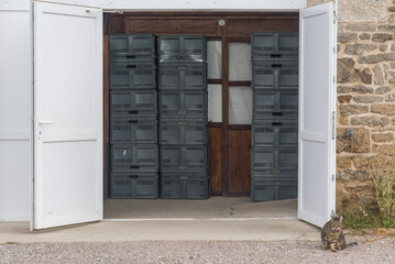 une porte blanche ouverte sur un entrepôt de caisses. Un chat devant une porte industrielle.