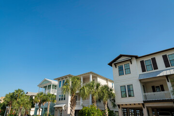 Fototapeta na wymiar Row of three-storey houses in Destin, Florida with wood sidings and parking space under. There is a house from the right with white and brown exterior along with houses with plants and trees at front.