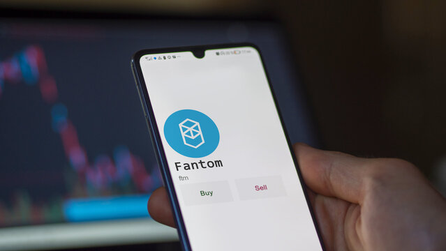 An investor's analyzing the fantom coin on screen. A phone shows the crypto's prices to invest in ftm