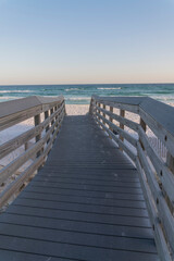 Wooden sloped walkway with railings heading to the beach with white sand in Destin, Florida. Seascape with horizon skyline view from a boardwalk.