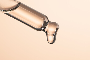 Glass dropper with liquid essential oil, serum dripping. Beauty background with skin and body care product, macro.