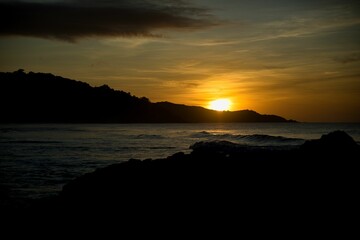 Picturesque sunset on the beach of El Nido, Palawan in the Philippines, the whole sky glows in golden yellow colors, hills on the horizon.