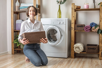Woman is washing white clothes in a washing machine in a laundry room. The concept of caring for things, cleaning and hygiene