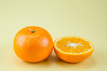 Fresh oranges and oranges cut in half isolated on soft yellow background