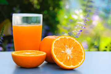 Cut oranges in half, oranges and orange  juice in  clear glass are placed on the side with beautiful blur  nature  flower and bokeh in the background