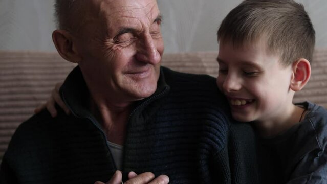 happy caucasian grandfather with grandson hugging smiling while sitting at home. friendship between grandfather and grandson, family relationships, emotions of people in the family
