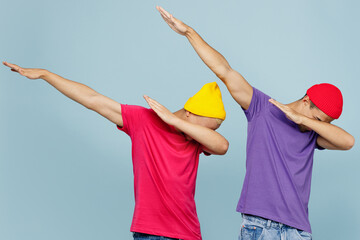 Young cool couple two friends men wear casual clothes together doing dab hip hop dance hand move gesture youth sign hide cover face isolated on pastel plain light blue cyan background studio portrait