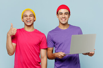 Young smiling satisfied couple two friends IT men wearing casual clothes together hold use work on laptop pc computer show thumb up isolated on pastel plain light blue cyan background studio portrait.